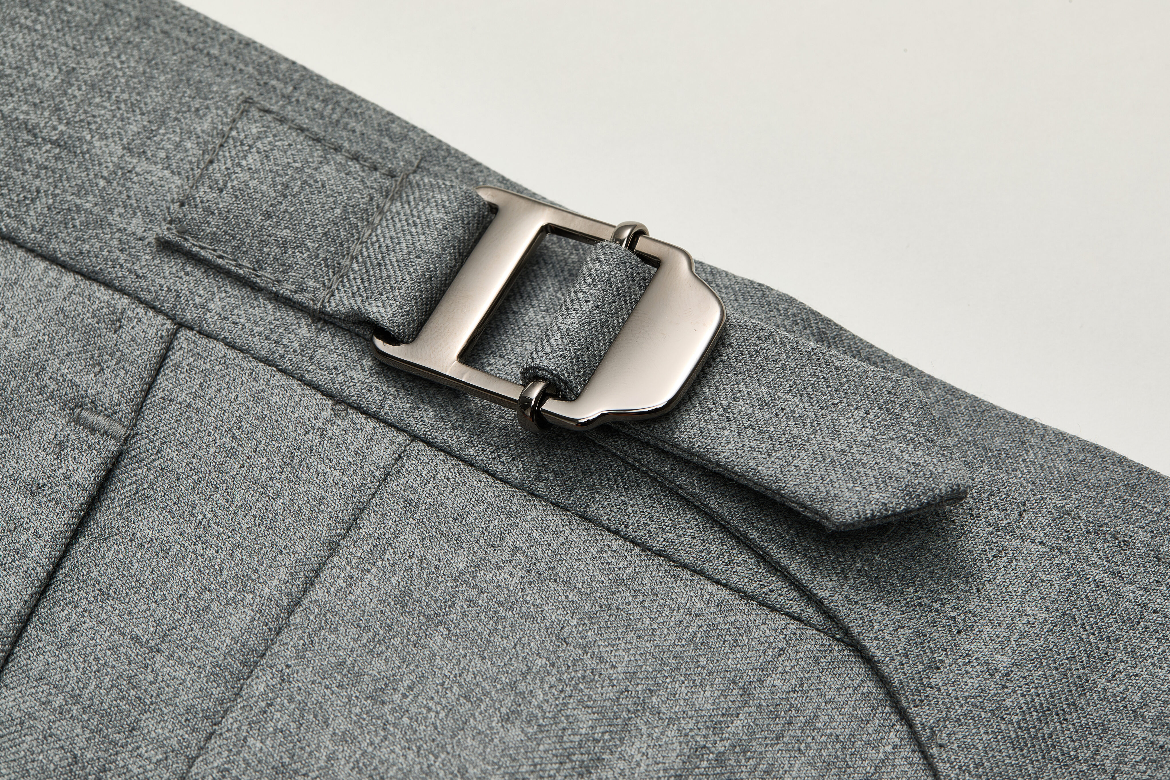 Side tab waistband adjustment detail on grey trousers.